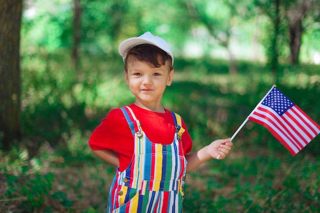 Uśmiechnięty chłopiec z dzieckiem flaga usa w jasnych ubraniach i białej czapce z flagą ameryki w dłoniach