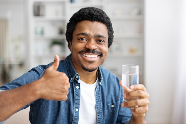 Uśmiechnięty czarny mężczyzna podnosi kciuk, trzymając szklankę wody.