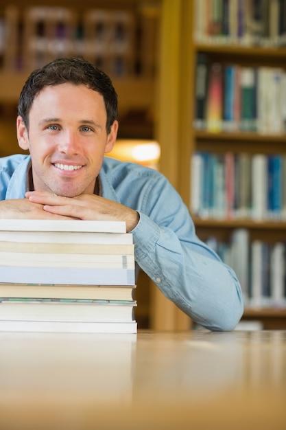 Uśmiechnięty dojrzały uczeń z stertą książki przy bibliotecznym biurkiem