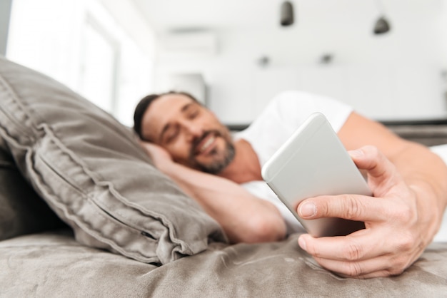 Uśmiechnięty dorośleć mężczyzna używa telefon komórkowego podczas gdy odpoczywający