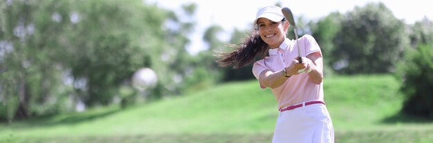 Uśmiechnięty dorosły kaukaski kobieta w klubie golfowym uderzając na portret piłki.