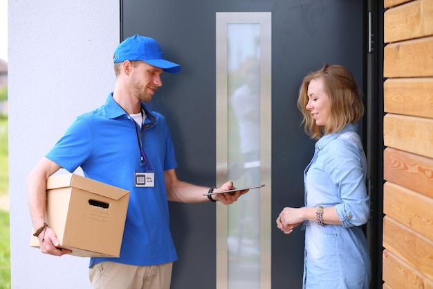 Uśmiechnięty dostawca w niebieskim mundurze dostarczający paczkę do koncepcji usługi kurierskiej odbiorcy