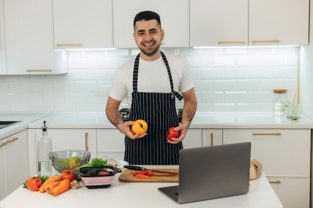 Uśmiechnięty facet przygotowuje warzywa w kuchni ubrany w czarny fartuch