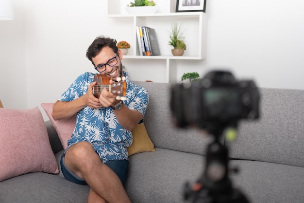 Uśmiechnięty i mrugający mężczyzna pozuje z ukulele w żywym pokoju dla kamery