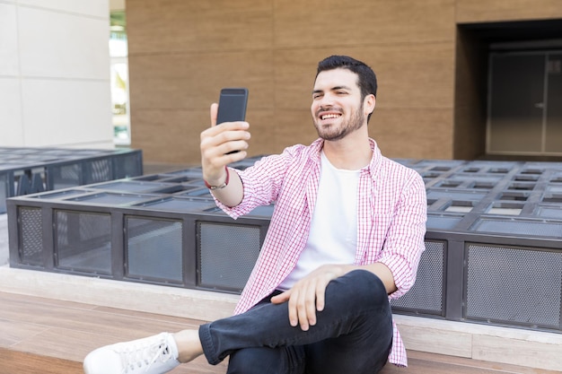 Uśmiechnięty Influencer Transmitujący Na żywo Na Smartfonie, Siedząc W Centrum Handlowym