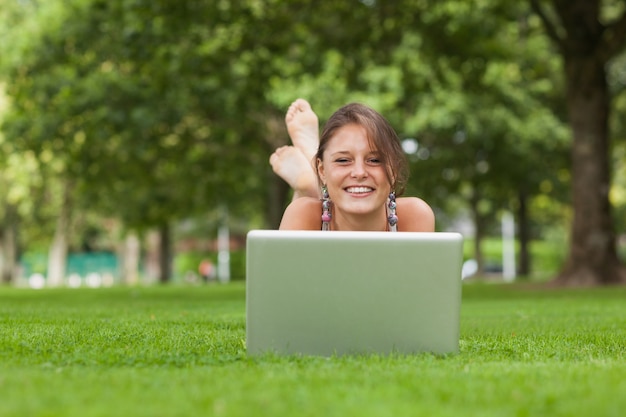 Uśmiechnięty kobiety lying on the beach na trawie i używać laptopie