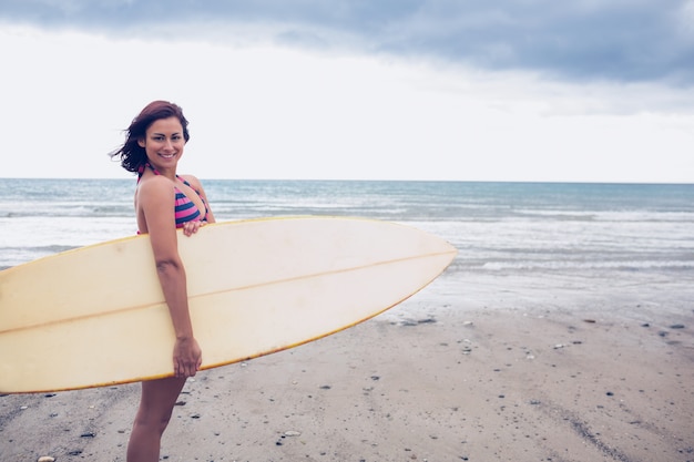 Uśmiechnięty kobiety przewożenia surfboard na plaży