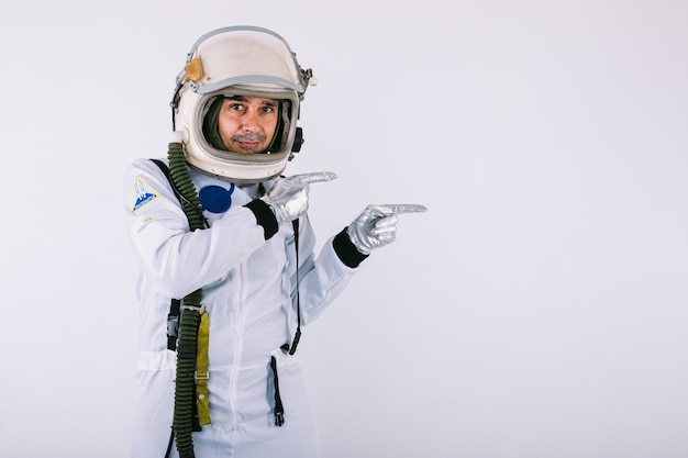 Uśmiechnięty kosmonauta mężczyzna w skafandrze i hełmie, wskazując ręką w prawo, na białym tle.