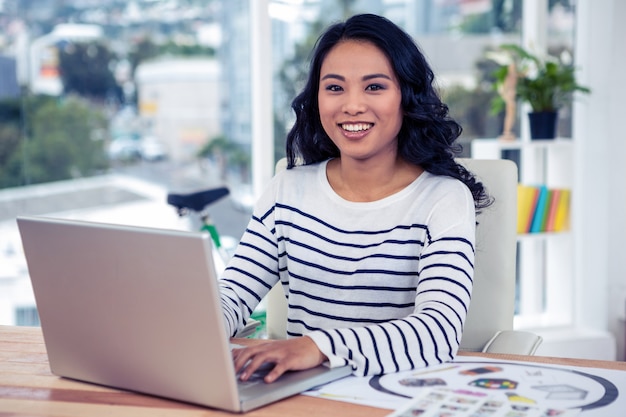 Uśmiechnięty kreatywnie bizneswoman używa laptop w biurze