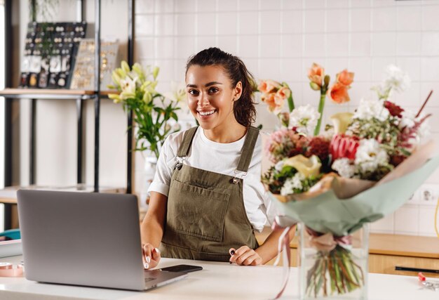 Uśmiechnięty kwiaciarz pracuje na laptopie przy kasie w sklepie