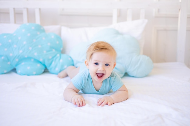 Zdjęcie uśmiechnięty lub śmiejący się chłopiec na łóżku w domu w niebieskich ubraniach obudził się rano lub idzie spać szczęśliwe dzieciństwo i rodzina