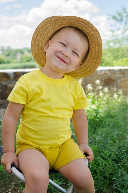 Uśmiechnięty mały chłopiec w naturze w słomkowym kapeluszu i żółtej koszulce słoneczne lato