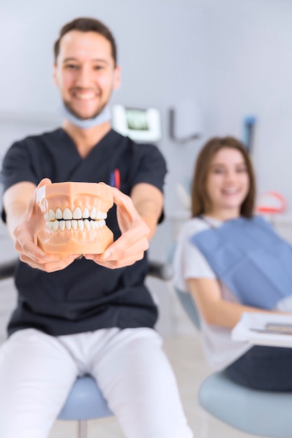 Uśmiechnięty męski dentysta pokazuje zęby model siedzi przed żeńskim pacjentem