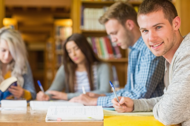 Uśmiechnięty Męski Uczeń Z Przyjaciółmi Przy Bibliotecznym Biurkiem