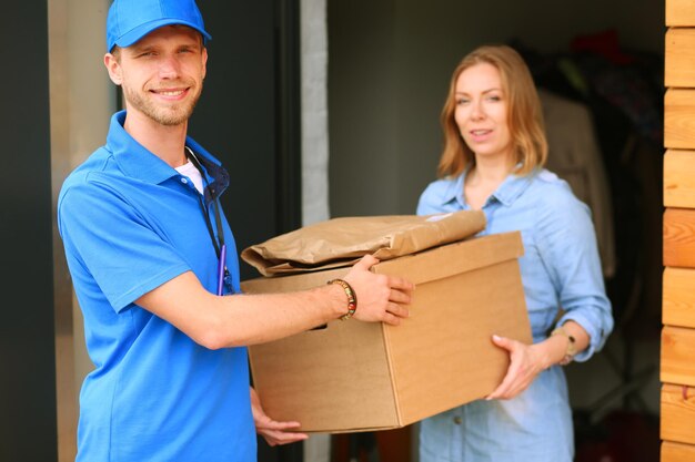 Uśmiechnięty mężczyzna dostawy w niebieskim mundurze dostarczający pudełko do odbiorcy koncepcji usługi kurierskiej Uśmiechnięty mężczyzna dostawy w niebieskim mundurze