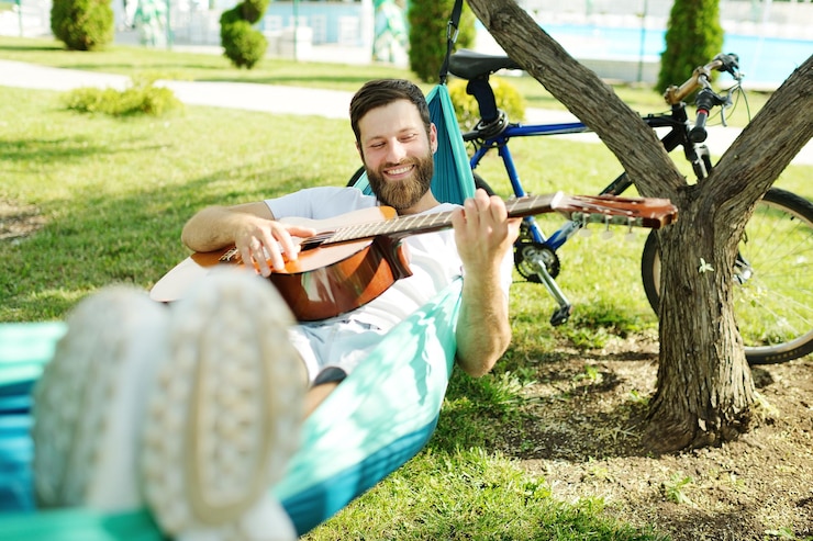 Zdjęcie uśmiechnięty mężczyzna grający na gitarze leżący na hamaku
