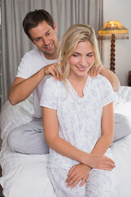 Uśmiechnięty mężczyzna masuje kobieta ramiona w łóżku