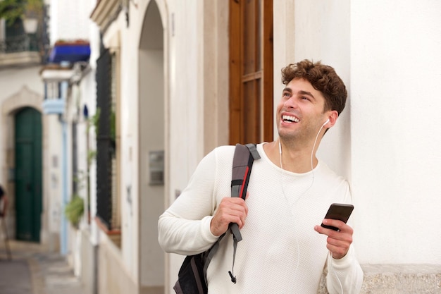 Uśmiechnięty mężczyzna mienia telefon komórkowy z plecakiem i hełmofonami