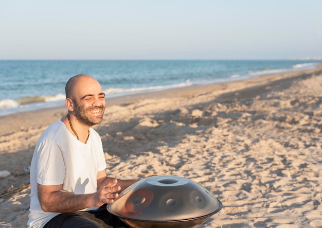 Uśmiechnięty mężczyzna muzyk grający na instrumencie handpan na plaży