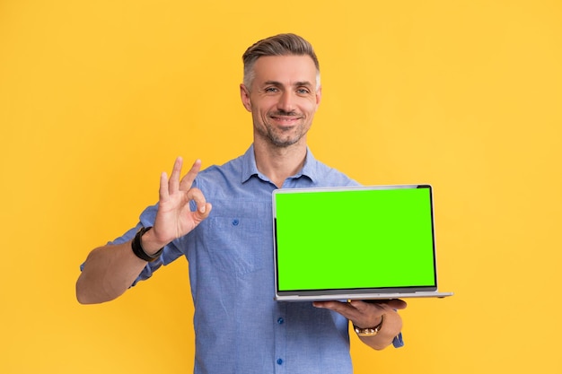 Uśmiechnięty mężczyzna przedstawiający komputer webinarowy pokazujący ok gest na żółtym tle kopia przestrzeń zakupy