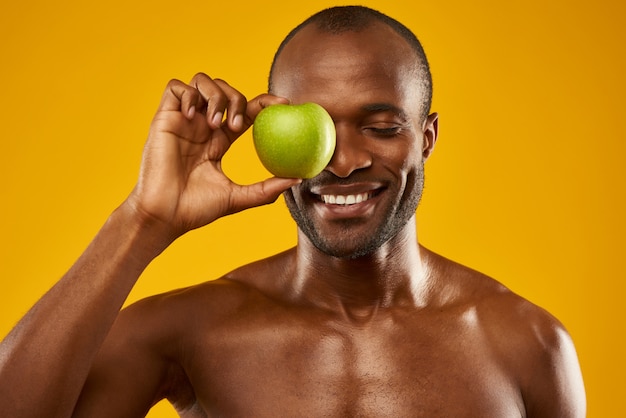 Uśmiechnięty mężczyzna trzyma jabłko przed zamkniętymi oczami