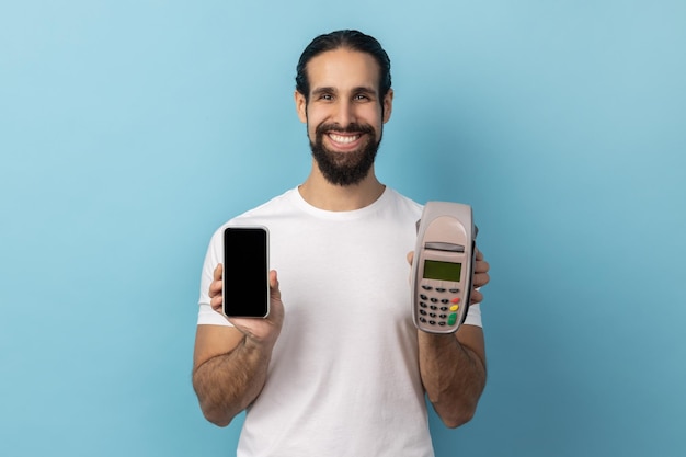 Uśmiechnięty mężczyzna trzymający terminal pos i inteligentny telefon z pustym wyświetlaczem na reklamę