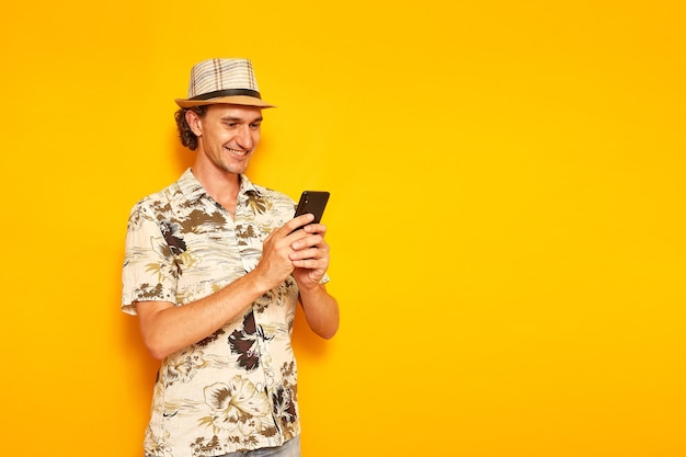 Uśmiechnięty Mężczyzna Turysta Na Wakacjach Z Telefonem W Rękach Pisze Wiadomość Na Białym Tle Na żółtym Tle