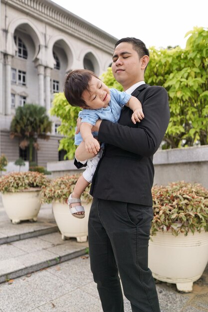 Uśmiechnięty mężczyzna w garniturze trzymający syna na zewnątrz