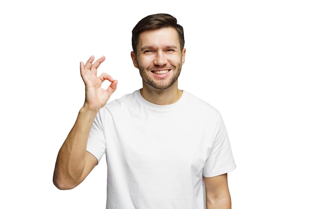 Uśmiechnięty mężczyzna z krótkimi włosami robi OK w pomieszczeniu w zwykłej białej koszulce