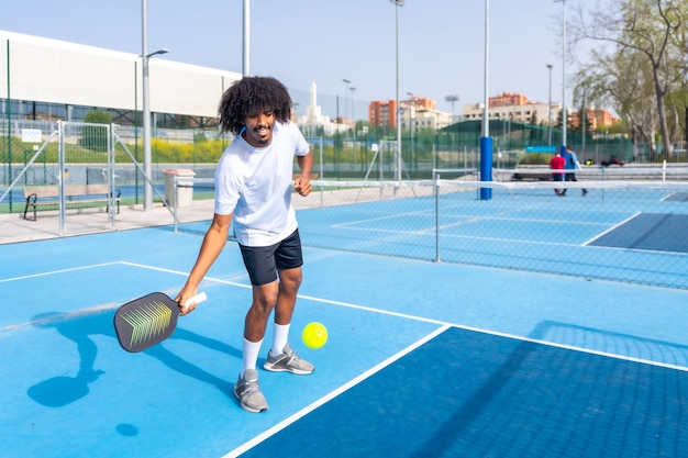 Zdjęcie uśmiechnięty mężczyzna z włosami afro służący podczas gry w pickleball