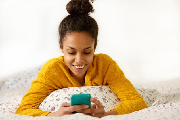 Uśmiechnięty młodej kobiety obsiadanie w łóżku z telefonem komórkowym
