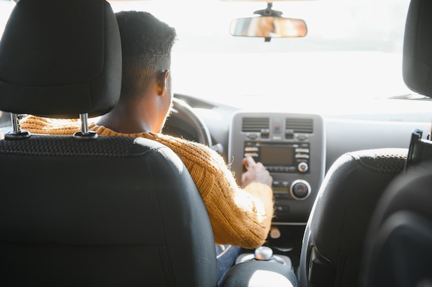 Uśmiechnięty młody Afroamerykanin siedzący w kabinie wygodnego nowoczesnego samochodu elektrycznego i dotykający ekranu nawigacji samojezdnego autopilota