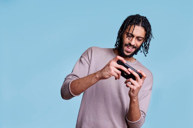 Zdjęcie uśmiechnięty młody arab grający w gry wideo na smartfonie i dobrze się bawiący. wesoła osoba korzystająca z zabawnej aplikacji na telefon komórkowy, ciesząca się rozrywką online