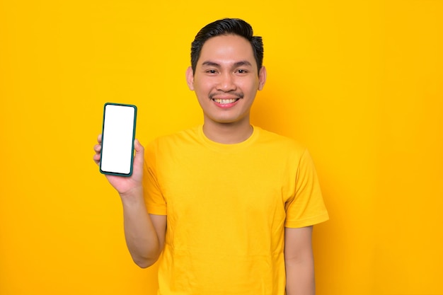Uśmiechnięty młody Azjata w casualowej koszulce pokazujący pusty ekran telefon komórkowy na żółtym tle Koncepcja stylu życia ludzi