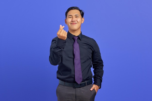 Uśmiechnięty młody azjatycki mężczyzna pokazujący znak gestu miłości na fioletowym tle