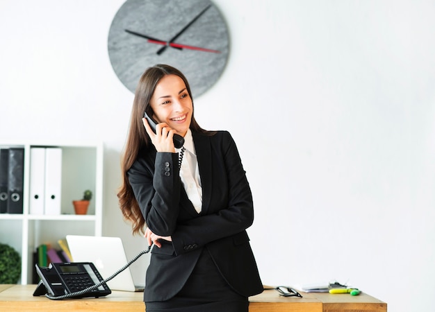 Zdjęcie uśmiechnięty młody bizneswoman ruchliwie w opowiadać na telefonie w biurze