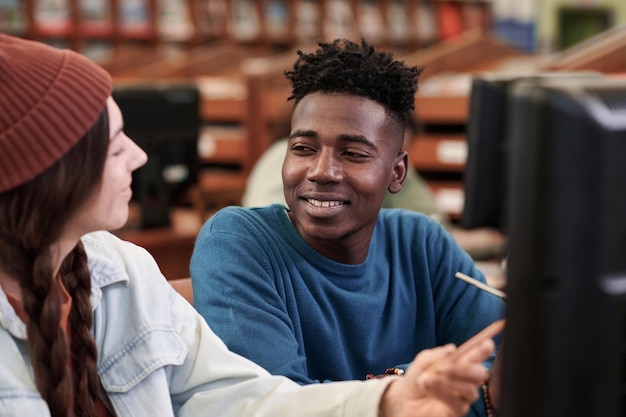 Uśmiechnięty młody czarny mężczyzna rozmawia z przyjacielem w bibliotece.