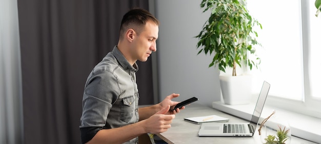 Uśmiechnięty młody człowiek freelancer za pomocą laptopa, studiujący online, pracujący w domu, szczęśliwy przypadkowy facet piszący na komputerze notebook surfujący po Internecie, cieszący się odległą pracą, siedzieć przy stole.