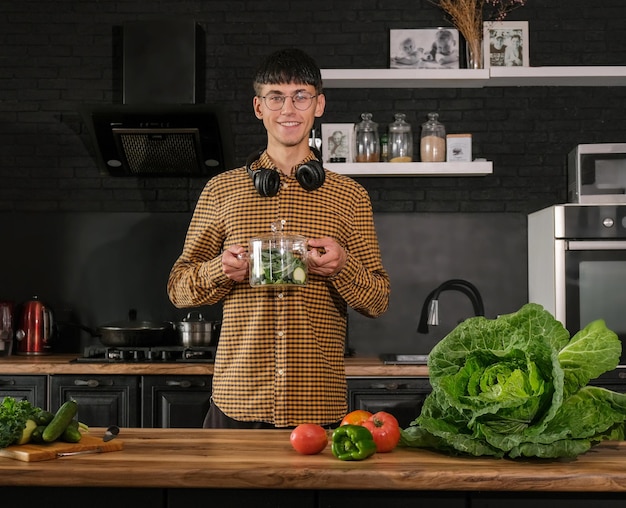 Uśmiechnięty młody człowiek gotuje sałatkę, kroi świeże warzywa w nowoczesnej czarnej kuchni