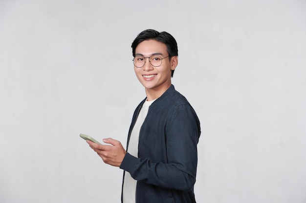 Uśmiechnięty młody człowiek patrząc na swojego inteligentnego telefonu podczas przesyłania wiadomości tekstowych na białym tle