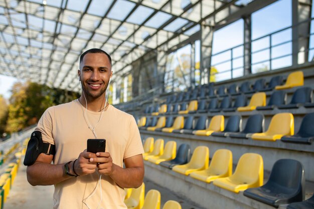 Uśmiechnięty młody człowiek sportowiec biegacz sportowiec stoi między trybunami na stadionie on