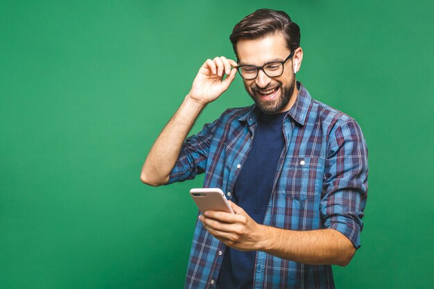 Zdjęcie uśmiechnięty młody człowiek trzyma mądrze telefon i patrzeje je. portret szczęśliwy mężczyzna używa telefon komórkowego odizolowywającego nad zielonym tłem.