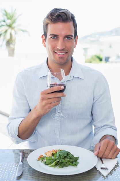 Zdjęcie uśmiechnięty młody człowiek z wina szkłem ma jedzenie