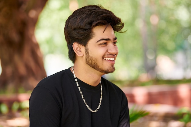 Uśmiechnięty młody indianin portret w czarnej koszulce i srebrnym łańcuszku na szyję odkryty zielony park publiczny