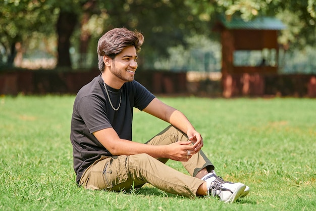 Uśmiechnięty młody indianin szczery portret w czarnej koszulce ze srebrnym łańcuszkiem na szyję, siedzący na zielonym trawniku