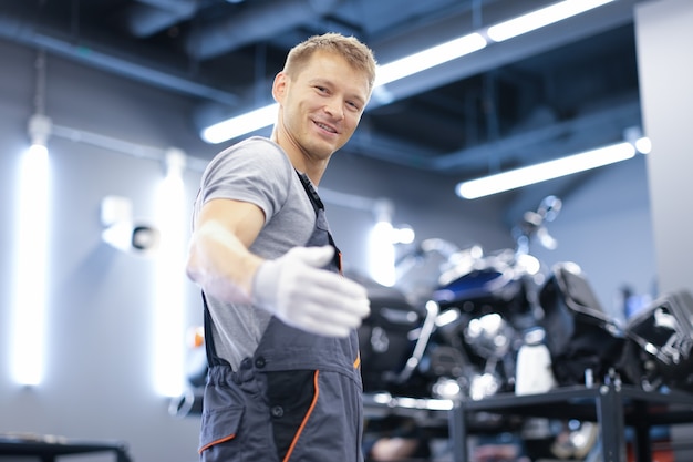 Uśmiechnięty młody mechanik samochodowy stoi w zbliżeniu warsztatu