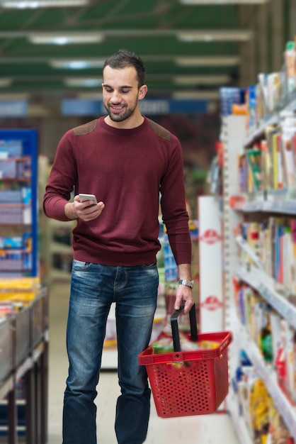 Uśmiechnięty młody mężczyzna korzystający z telefonu komórkowego podczas zakupów w sklepie zakupowym