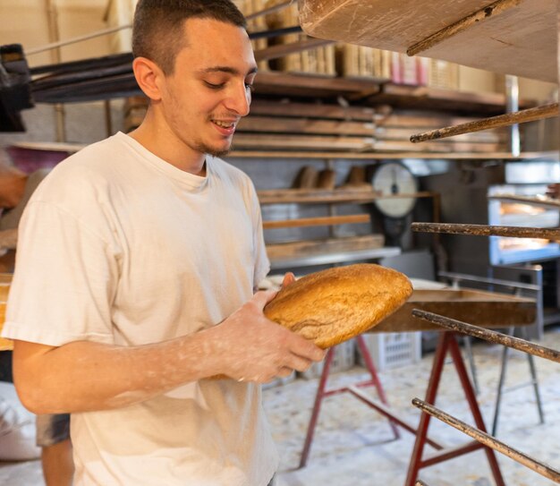 Uśmiechnięty młody piekarz trzyma pieczony przez niego chleb