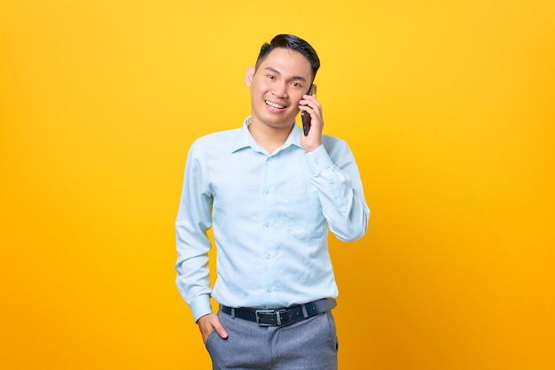 Uśmiechnięty młody przystojny biznesmen rozmawia przez smartfon na żółtym tle