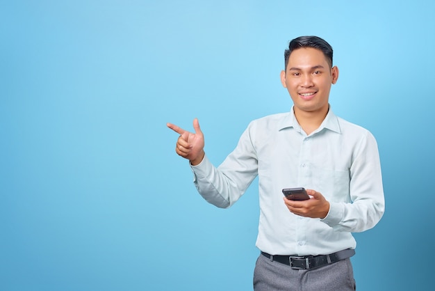 Uśmiechnięty młody przystojny biznesmen trzymający smartfon i wskazujący palcem od miejsca kopiowania